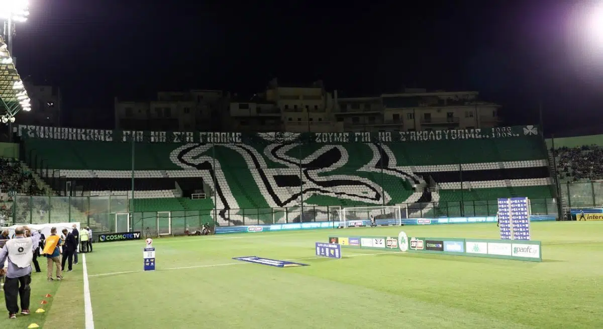 The empty stands of Apostolos Nikolaidis Stadium, decorated with a large green and white Panathinaikos emblem and a banner reading "Γεννηθήκαμε για να σε φωνάζουμε, ζούμε για να σε ακολουθούμε 1908